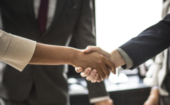 2 people shake hands (they are wearing professional business wear).