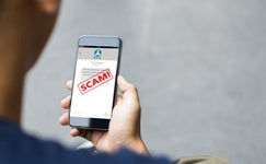 Person holding a phone with a text open, red SCAM over it