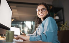 Person sitting at desk with computer, smiling at camera.