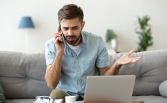 Person annoyed looking at their laptop, on phone with someone.
